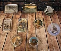 Top-down view of nine glass paperweights with various images including landscapes, portraits, and buildings on wooden background