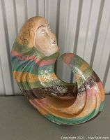 Photo showing front angle of the vintage lady sculpture with its multicolored striped body curled underneath the painted face.