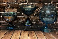 Photo showing three iridescent serving dishes and a large blue glass vase on a wood surface against a brick backdrop.