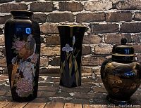 Photo showing three black ceramic vases with Asian-style floral and bird designs against a brick wall background.