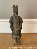 Front view of the Chinese terra cotta warrior figurine standing on a wooden surface against a plain light wall.