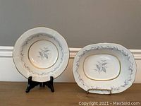 Two bowls displayed side by side on stands against neutral background, showing round and oval bowls with Morning Mist floral pattern and gold gilt trim.