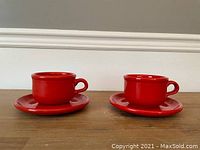 Photo of two red coffee cups with saucers placed side by side on a white surface.