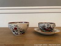 Photo of the decorative bowl and the tea cup on its saucer, showing their size, shape and detailed scenic oriental-inspired pattern in red, green, black, and orange with brown rims.