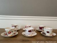 Front view of the six tea cups and saucers arranged on wooden surface, showing the floral patterns and delicate shape of cups and saucers.