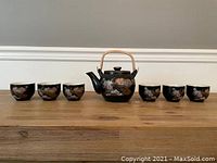 Full view of Japanese tea set on wooden surface showing teapot and six cups with peacock and floral motif.