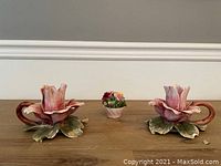 Front view of two pink floral porcelain candle holders with green leaves and one small floral bouquet centerpiece on wooden table.