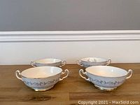 Four white porcelain soup cups with two handles each, decorated with gray floral pattern and gold rim and base.