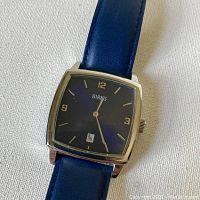 Close-up of Birks watch face showing blue rounded square dial, gold-tone hour markers, and date window at 6 o'clock.