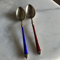 Pair of demitasse spoons photographed on marble surface showing the front with silver bowls and vibrant red and blue enamel handles