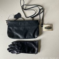 Black Derek Alexander leather purse with an adjustable strap and a pair of black leather gloves laid out on a white surface.