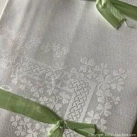 Close-up photo showing white double damask Irish linen napkin with detailed woven shamrock and Celtic knot design, tied with a green ribbon