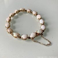 Bracelet laid flat on reflective surface showing overall design, 15 oval opals in gold prong settings.