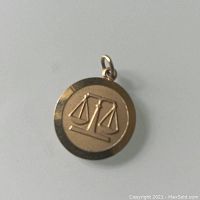Front view of circular gold charm with Libra scales symbol