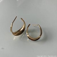 Pair of polished 14K gold half hoop earrings on a white surface, showing overall shape and condition.