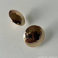 Two round hammered gold earrings shown on white background with visible stamped post backs.
