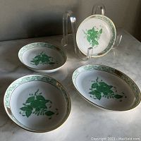 Four oval porcelain side dishes shown with front view highlighting hand painted green floral design and gold trim
