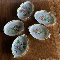 Top view showing five hand-painted Herend Hungary oval side dishes with floral designs and gold rim, laid out on wood surface.