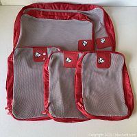 Overview of five zippered travel compartments arranged from largest to smallest, showing mesh fronts and red fabric borders with HEYES logo patches.