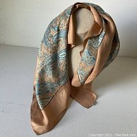 Full view of scarf draped to show color and pattern with peach border and turquoise paisley on silk fabric.