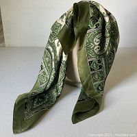 Silk scarf draped on a stand showing green paisley bordered design and drape quality