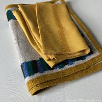 Set of folded linens showing golden yellow synthetic napkins on top of linen placemat with multicolored border