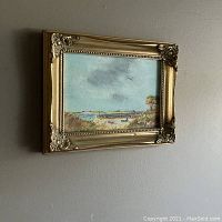 Full view of the framed original painting showing a beach scene under a blue sky hanging on a wall.