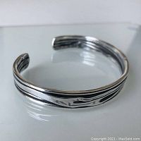 Silver cuff bracelet showing the front view with crinkled and oxidized recessed portions, reflecting Brutalist design style.
