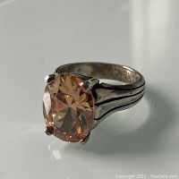 Close-up photo of the silver ring showing large orange-yellow oval faceted stone and triple groove band design