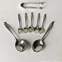 Pair of sugar tongs at top with five small demitasse spoons and two larger serving spoons below