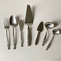 Seven silver plated serving pieces arranged side by side on neutral background.