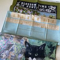 Six vintage linen tea towels stacked, showing floral and architectural prints.