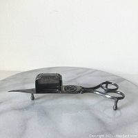 Side view of vintage silver plate wick trimmer with three small legs and scissor handle.