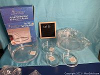 Six acrylic bowls shown with one large bowl in original box and three small bowls, all clear acrylic, along with a pair of clear acrylic tongs.