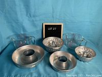 Four vintage angel food cake tins of varying sizes and two clear Pyrex measuring cups on blue cloth background.