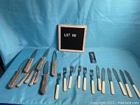 Assorted vintage cutlery laid out, including knives and forks with bone-like and wood handles on a blue cloth background.