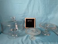 Three glass cake plates: one with clear glass dome lid and two detailed glass plates with designs