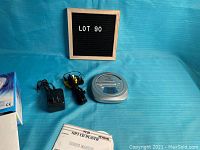 Photo shows Aftron CD/MP3 player, power adapter, wired headphones, and folded user manual against a blue background with lot sign.