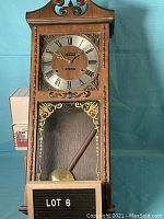 Front view of Citizen 31 Day wall clock showing wooden carved frame, clock face with Roman numerals, and glass panel with brass pendulum inside