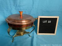 Copper chafing dish fully assembled with lid and sterno holder visible underneath on brass legs.