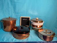Four copper pots including a large tall pot, a brand new pot with lid, an amber Pyrex covered saucepan, and a fondue pot with white insert.