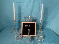 Photo showing entire lot of crystal items arranged behind a Lot 8 sign, including candle holders, vase, bell, condiment dish, and creamer.