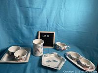 Full view of the four pottery pieces arranged on a blue cloth background, including square plate, small vase, gravy boat, and divided dish.