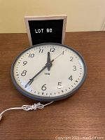 Photo of the vintage IBM wall clock lying flat on a wooden surface showing the front face, cord, and switches.