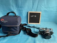 Photo showing Konica Autoreflex T camera with attached lens and Lowepro carrying case alongside a small board indicating lot number 79.