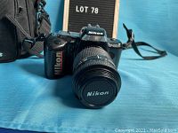 Front angle view of Nikon F-401s camera with Nikon lens and lens cap attached, Nikon logo visible on lens cap and camera top.