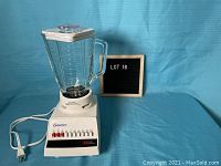 Full view of white Osterizer blender on blue background with jar and lid in place