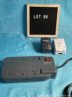 Photo of two Ethernet over Powerline adapters and a power strip on blue background with 'LOT 88' board.
