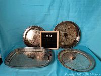 Four silverplate serving trays displayed against a blue backdrop, showing different sizes and styles with tarnish visible.