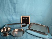 Five assorted stainless steel serving dishes arranged together, various shapes and sizes visible, some with wooden handles